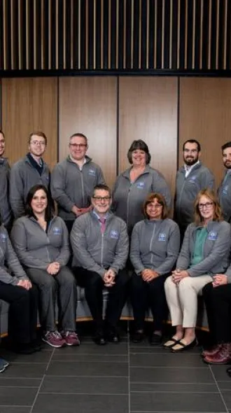 The RADOR-KY research team in matching grey jackets. They are gathered in two, overlapping  semi-circles, with the front row sitting down, and the back row standing.