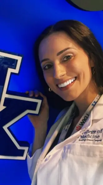 Alicia, in a white coat, poses next to a neon UK sign
