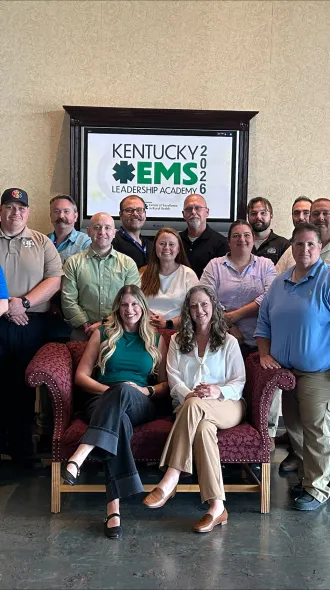 Kentucky EMS Leadership Academy 2026 graduates and mentors pose for a group photo in Kentucky, standing and seated in front of a wall-mounted academy sign displaying the 2026 program name.