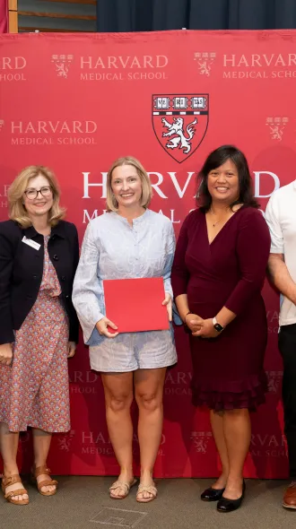 Image of 5 medical professionals at Harvard Medical School's SQIL program graduation with red Harvard College Logo in background. 