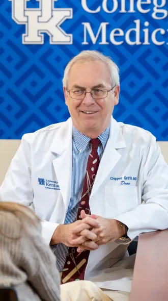 From left: The back of a woman's head as she sits and talks to  (right) Dean Griffith, wearing a white coat, smiling
