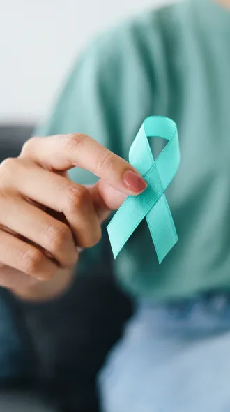 A closeup of a woman's hand, holding an ovarian cancer ribbon