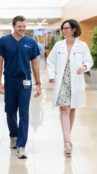 2 medical students in blue scrubs walk alongside an attending in a white coat 
