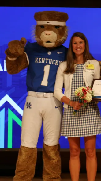Image of Chrissie Adams, CNM, holding award certificate and posing with Wildcat mascot. 