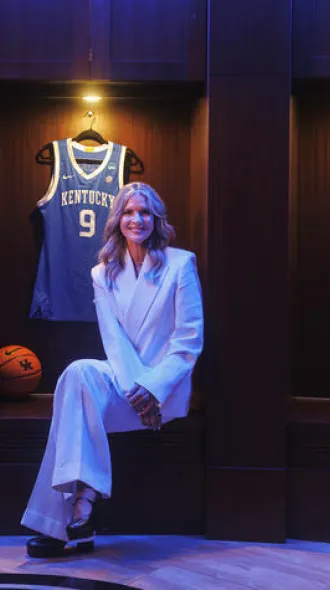 Lee Anne Pope sitting in a dramatically lit room with basketball jerseys hanging behind her on the wall.