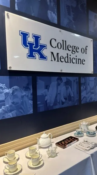 UK College of Medicine sign hangs above a table covered in white table cloth and set for a full tea time. 